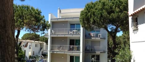 A multi-story residential building with balconies, surrounded by trees and a clear sky.