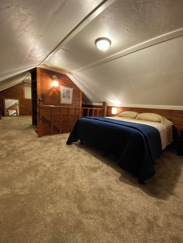 A bedroom with a sloped ceiling, a wooden staircase, a bed with a blue bedspread, and a wall-mounted light fixture. - Cozy Private Country House for Family & Friends Near La Crosse and Onalaska (Onalaska)