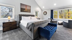 Ein Schlafzimmer mit einem großen Bett, einem Schminktisch, einer Bank und Blick auf Bäume durch das Fenster.