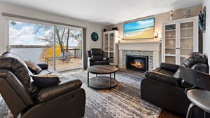 Ein modernes Wohnzimmer mit Ledersofas, einem Kamin, einem großen Fernseher und Blick auf einen See.