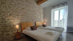 Een slaapkamer met twee bedden, stenen muren, houten balken en een groot raam.