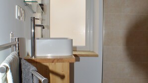 Een badkamer met een houten wastafelmeubel, een witte wastafel, een handdoekrek met handdoeken, een spiegel en een douchegedeelte met betegelde wanden.