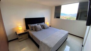 Quarto com cama, mesas de cabeceira, janela com vista e luminária no teto.