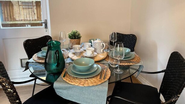 A dining area with a glass table set for four, surrounded by wicker chairs.