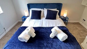 A neatly made bed with a blue headboard, white bedding, and two bedside lamps.