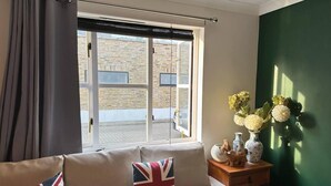 A room with a sofa, a window with blinds, a green wall, and a small wooden side table with decorative items.