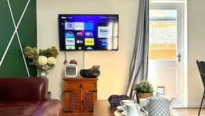 A living room with a leather sofa, a wooden coffee table with a tray holding a teapot and cups, and a flat-screen TV displaying streaming services.