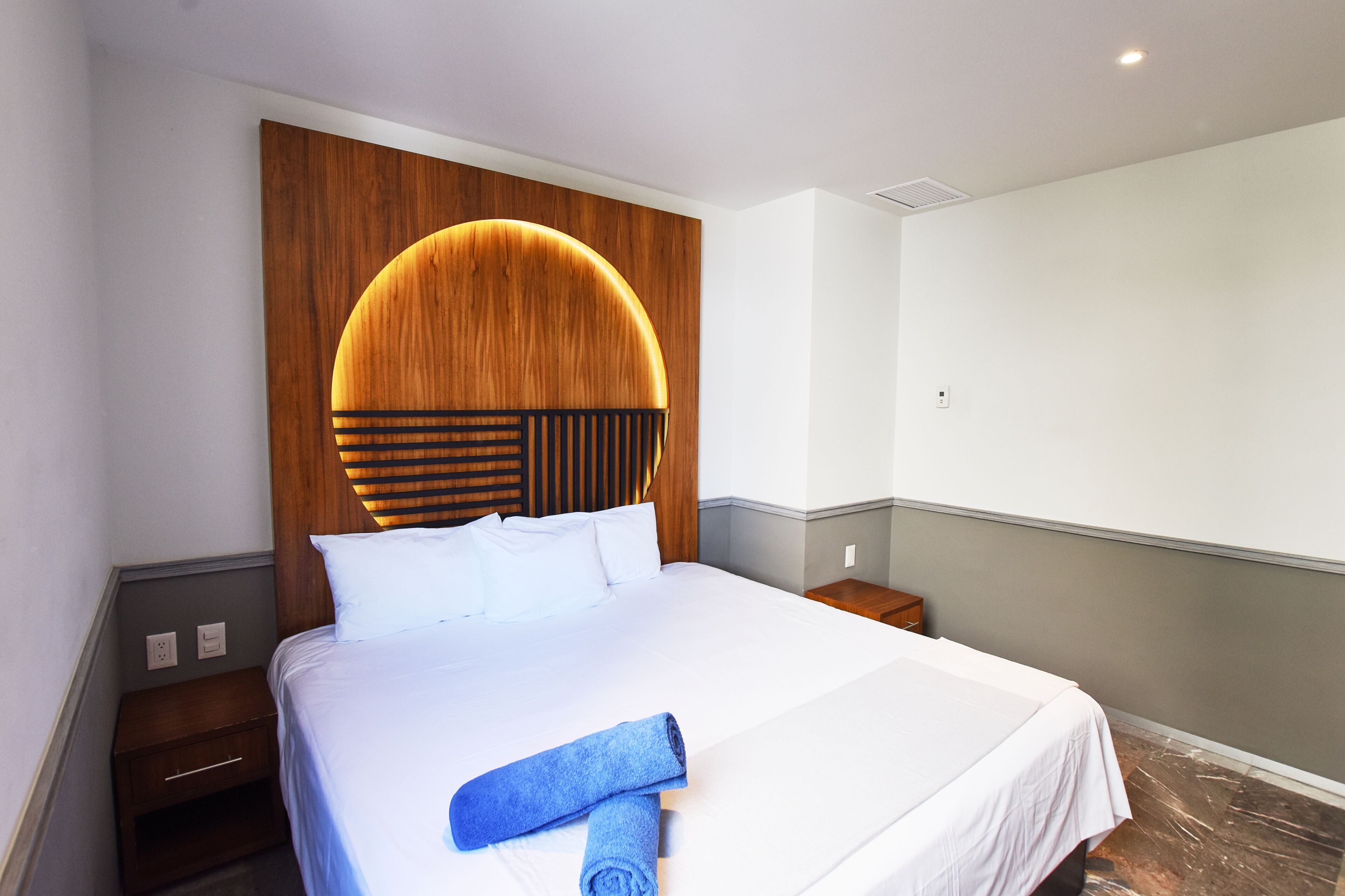 Hotellihuone, jossa on suuri sänky, puinen pääty, valkoiset vuodevaatteet ja sininen pyyhe sängyllä.