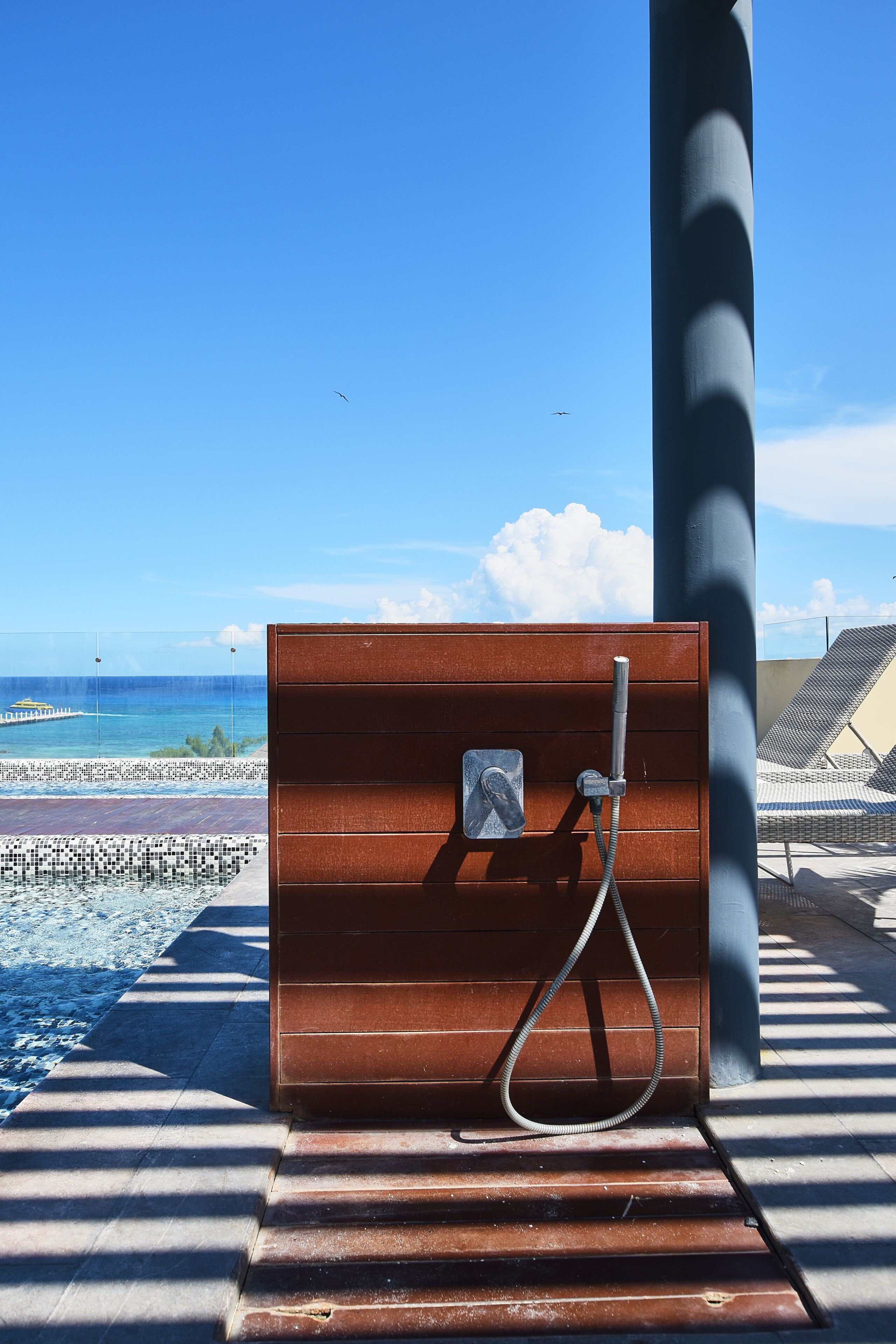 A shower enclosure with a view of the ocean and a pier in the background.