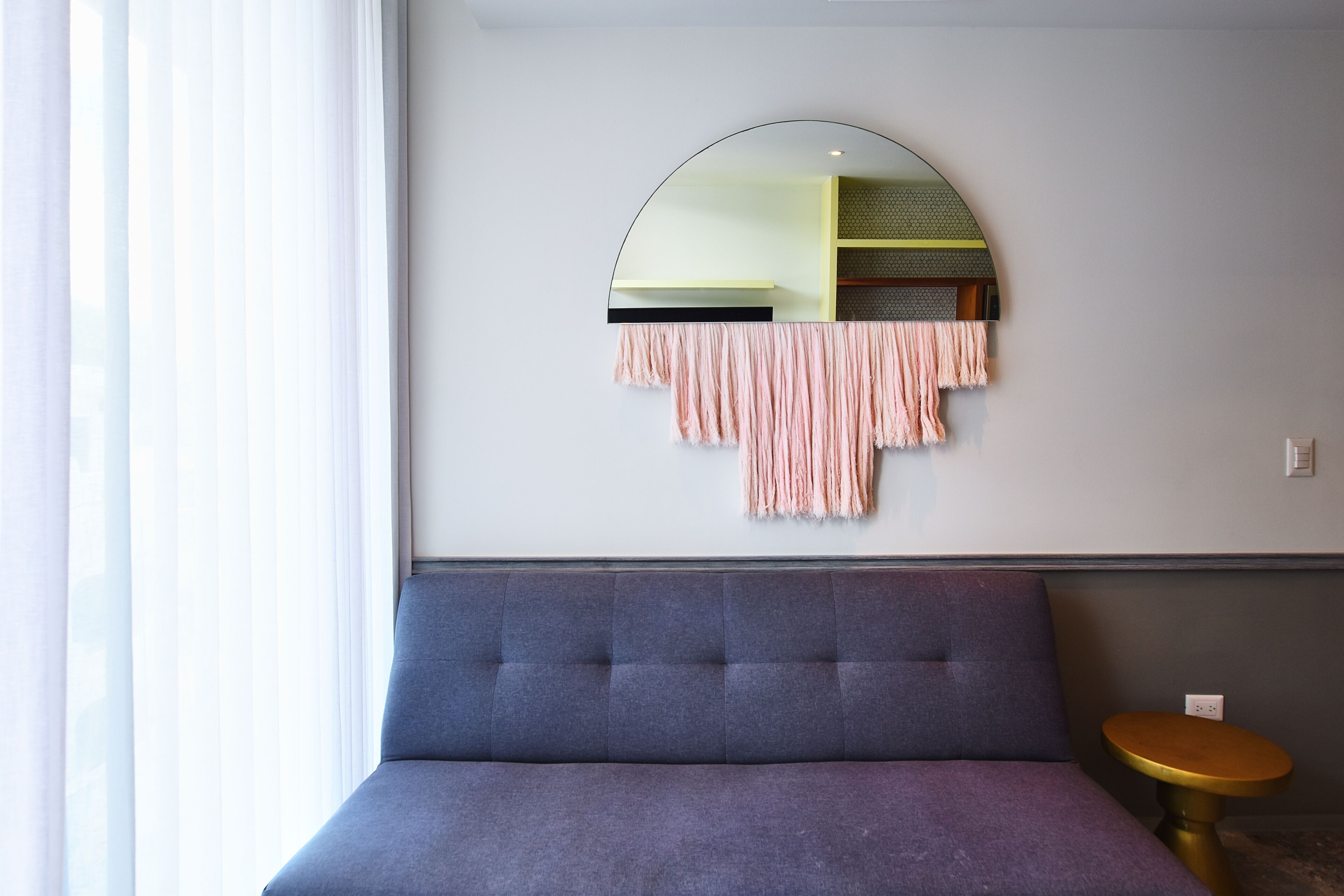 Una habitación con un sofá azul, un espejo redondo y una pequeña mesa de madera.