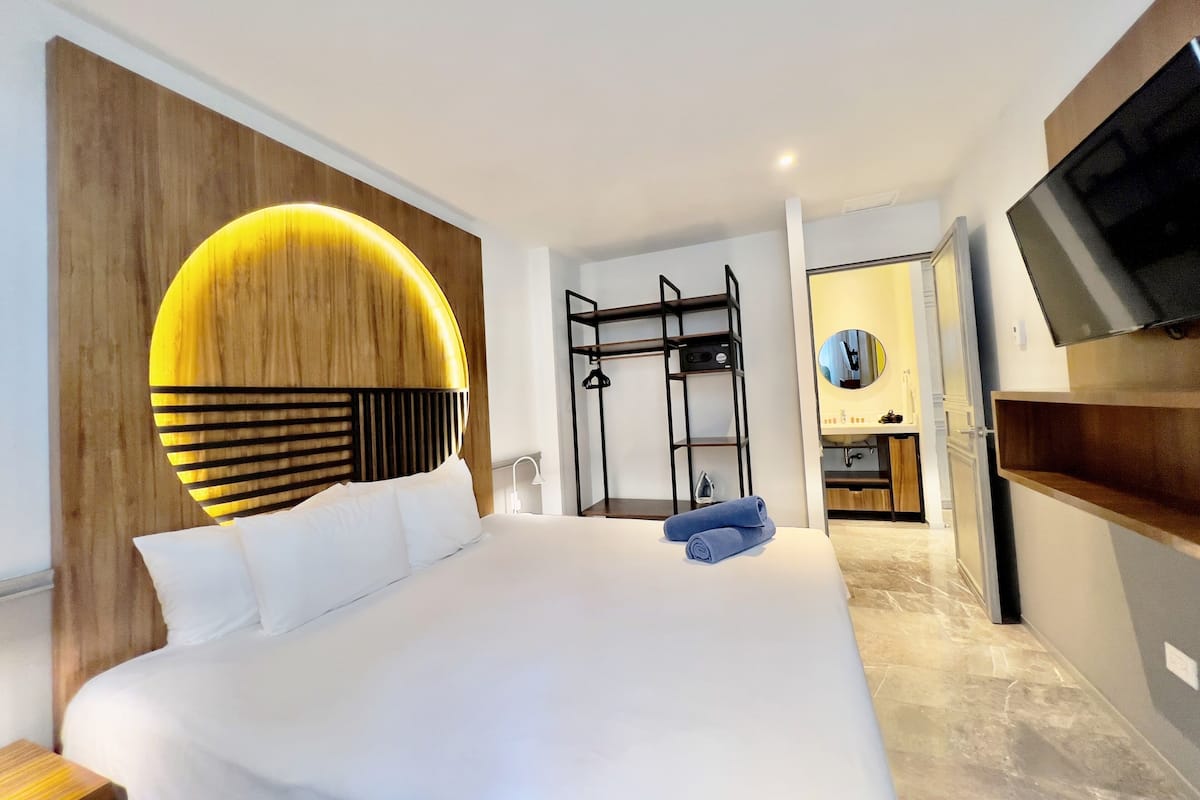 A modern hotel room with a large bed, a wooden accent wall, a built-in TV, and a walk-in closet.