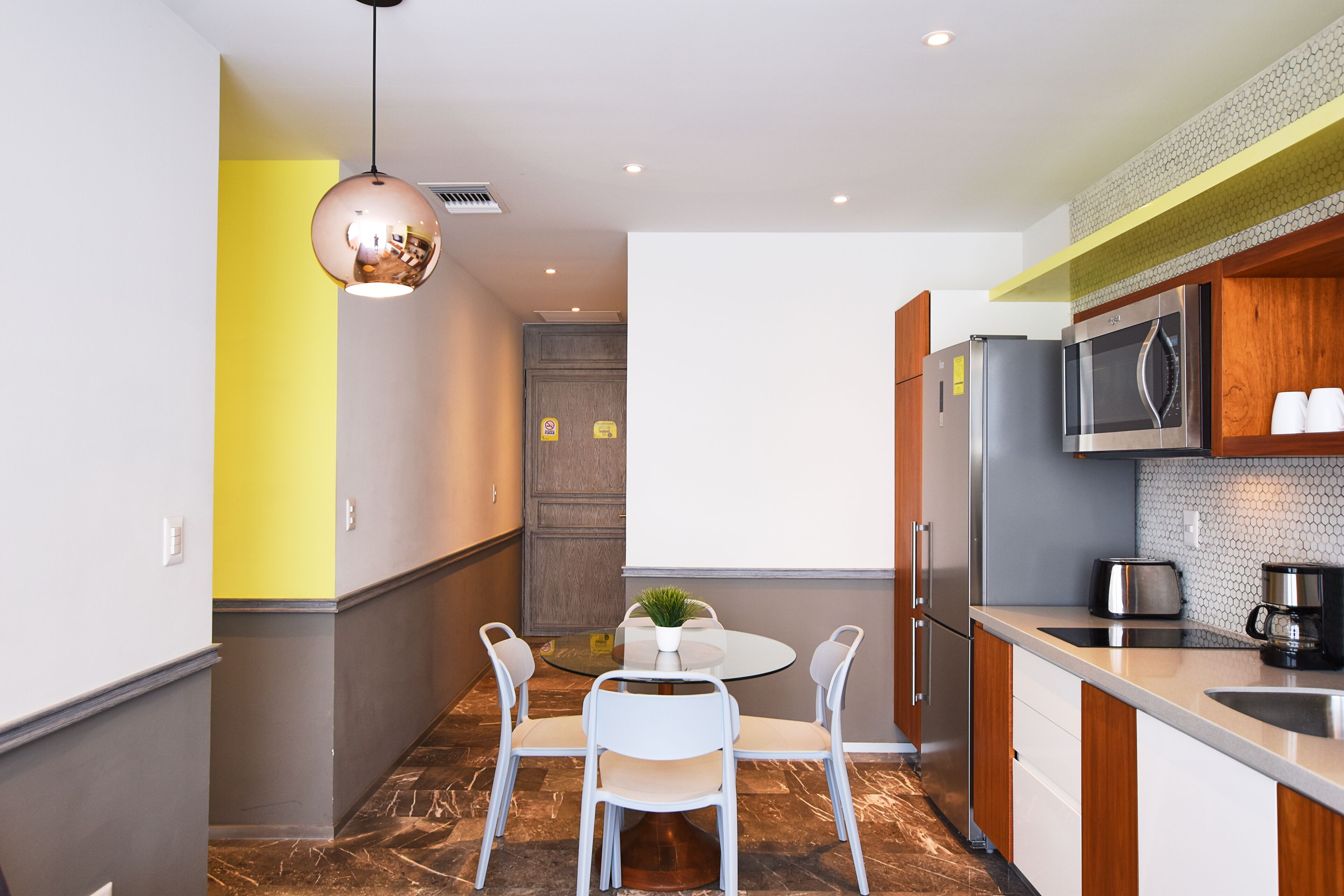 Una cocina moderna con una mesa redonda, sillas blancas, una lámpara colgante y electrodomésticos de acero inoxidable.