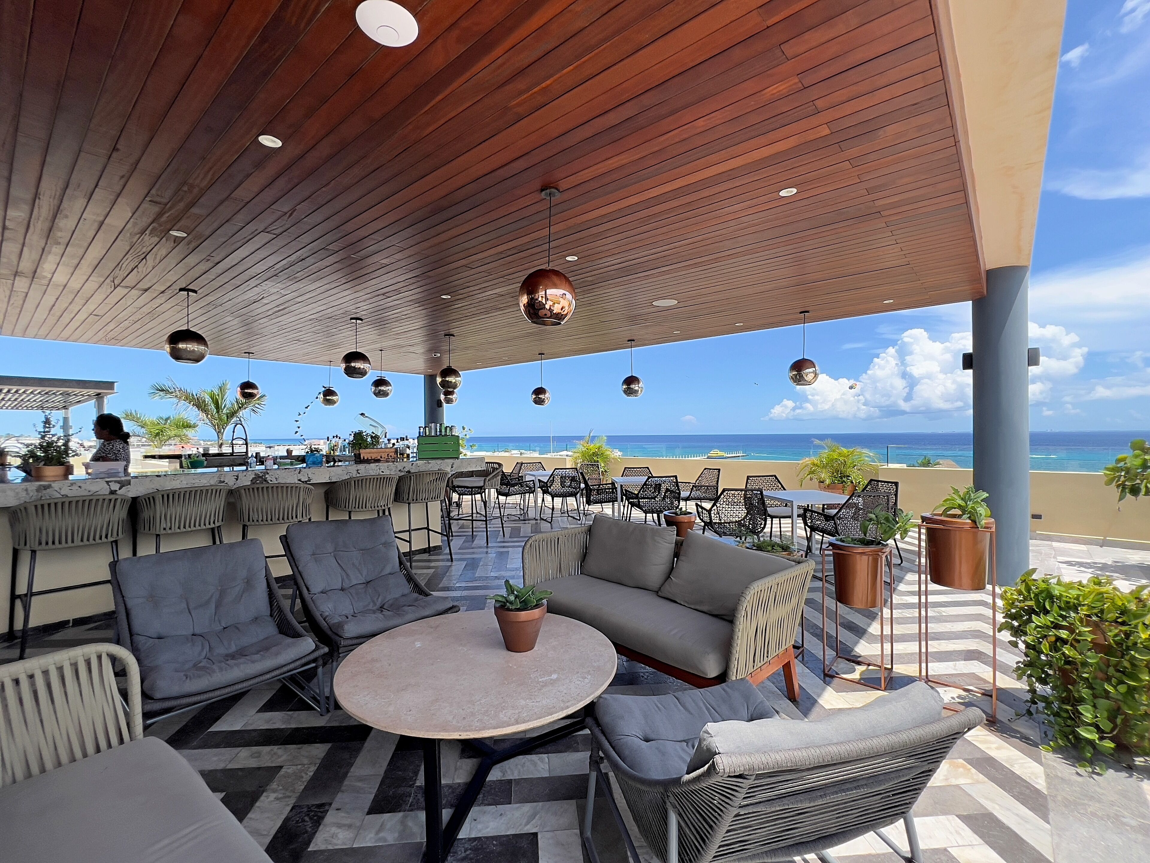A covered outdoor seating area with wicker furniture, a bar, and a view of the beach.