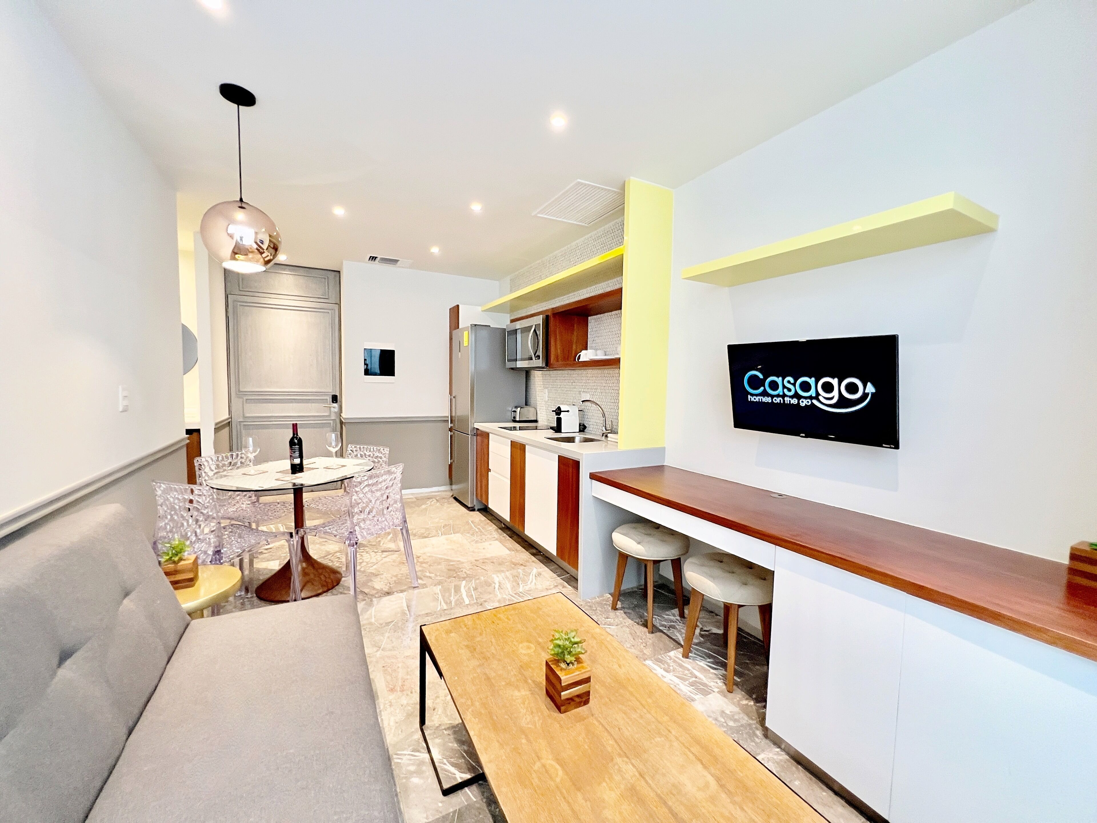 A modern kitchen with a flat-screen TV, a dining area with a round table and chairs, and a small seating area with a sofa and a wooden table.