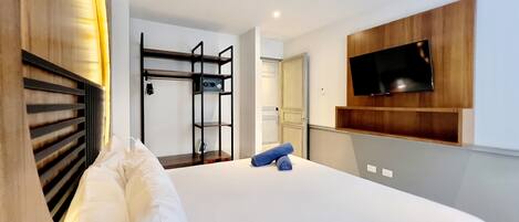 Ein Hotelzimmer mit einem Bett, einem an der Wand montierten Fernseher, einem Holzschrank und einem Kleiderständer.