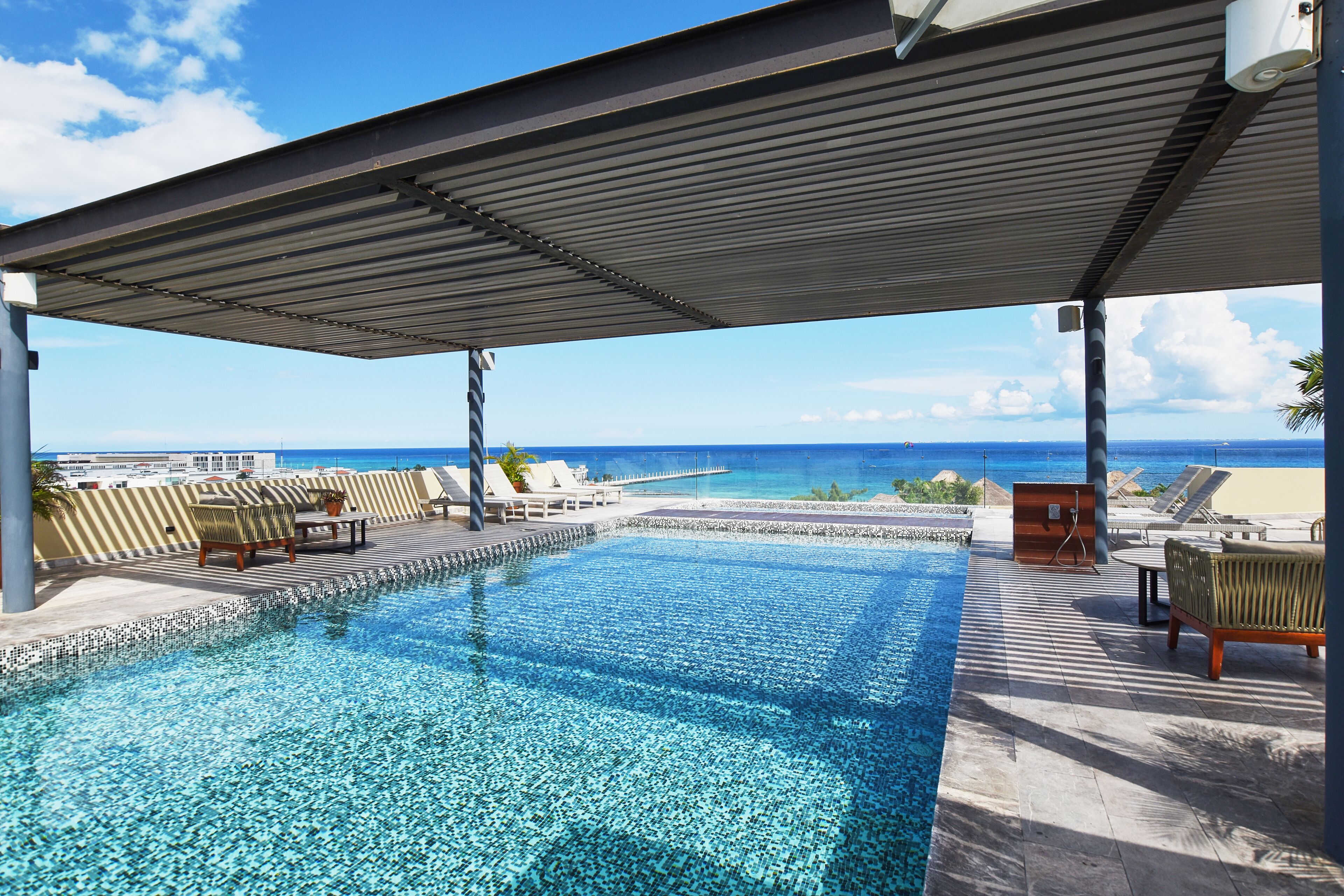 Área da piscina com vista para o oceano, cadeiras de descanso e um alpendre coberto.