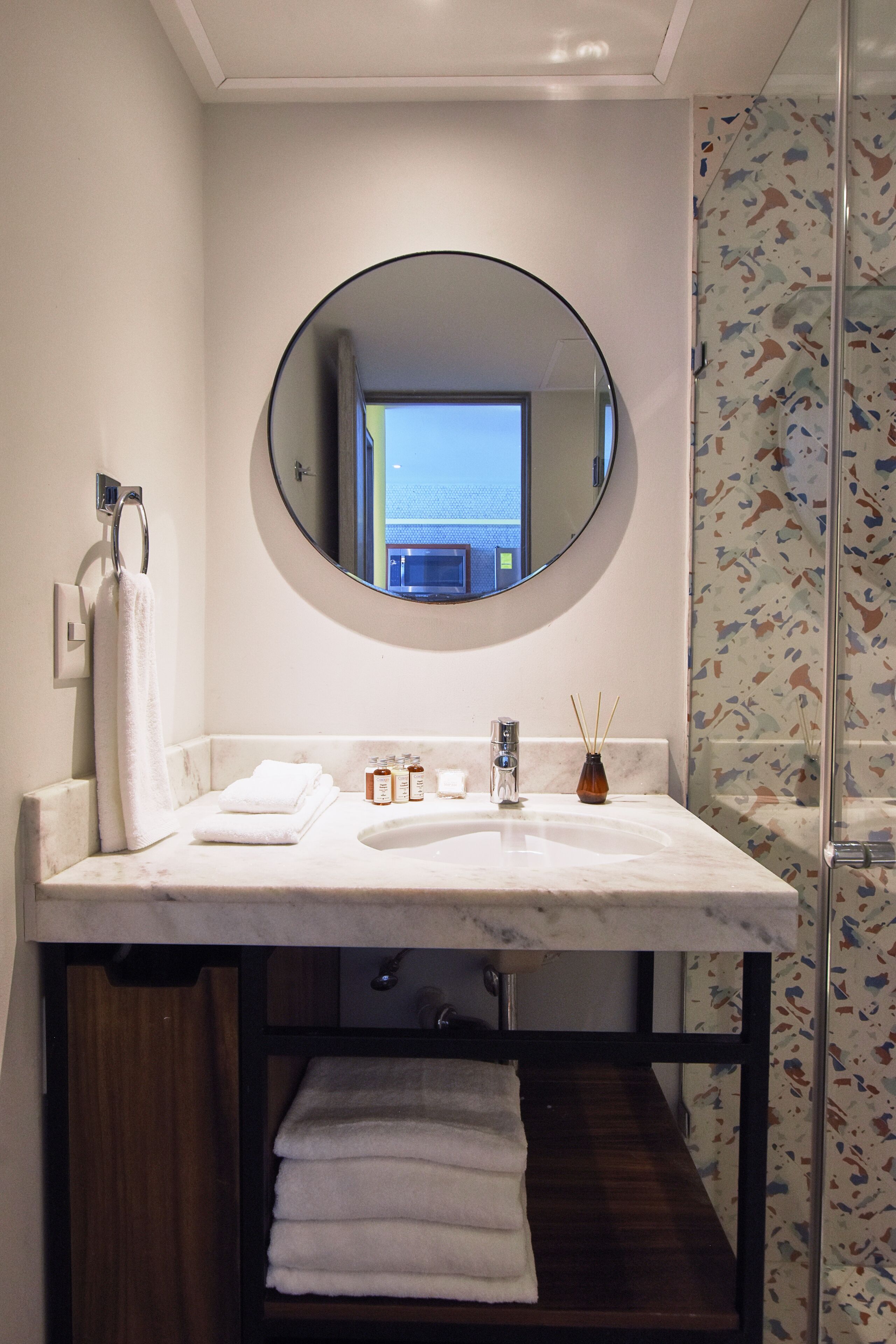 A bathroom with a round mirror, a sink, and a towel rack.