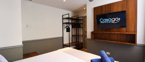 A hotel room with a bed, a TV mounted on the wall, and a wooden shelf below it.
