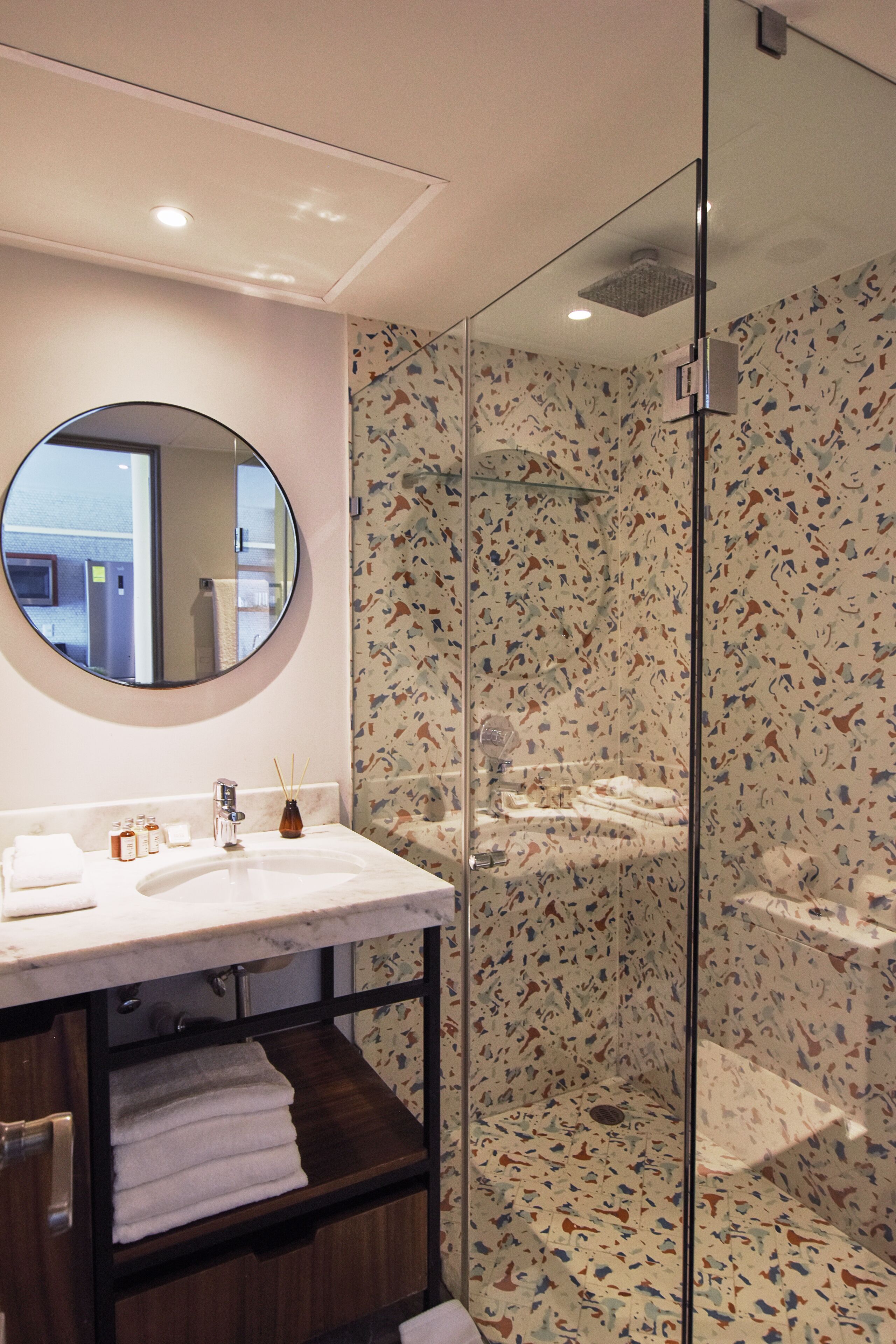 Een moderne badkamer met een ronde spiegel, een witte wastafel en een douchecabine van glas.