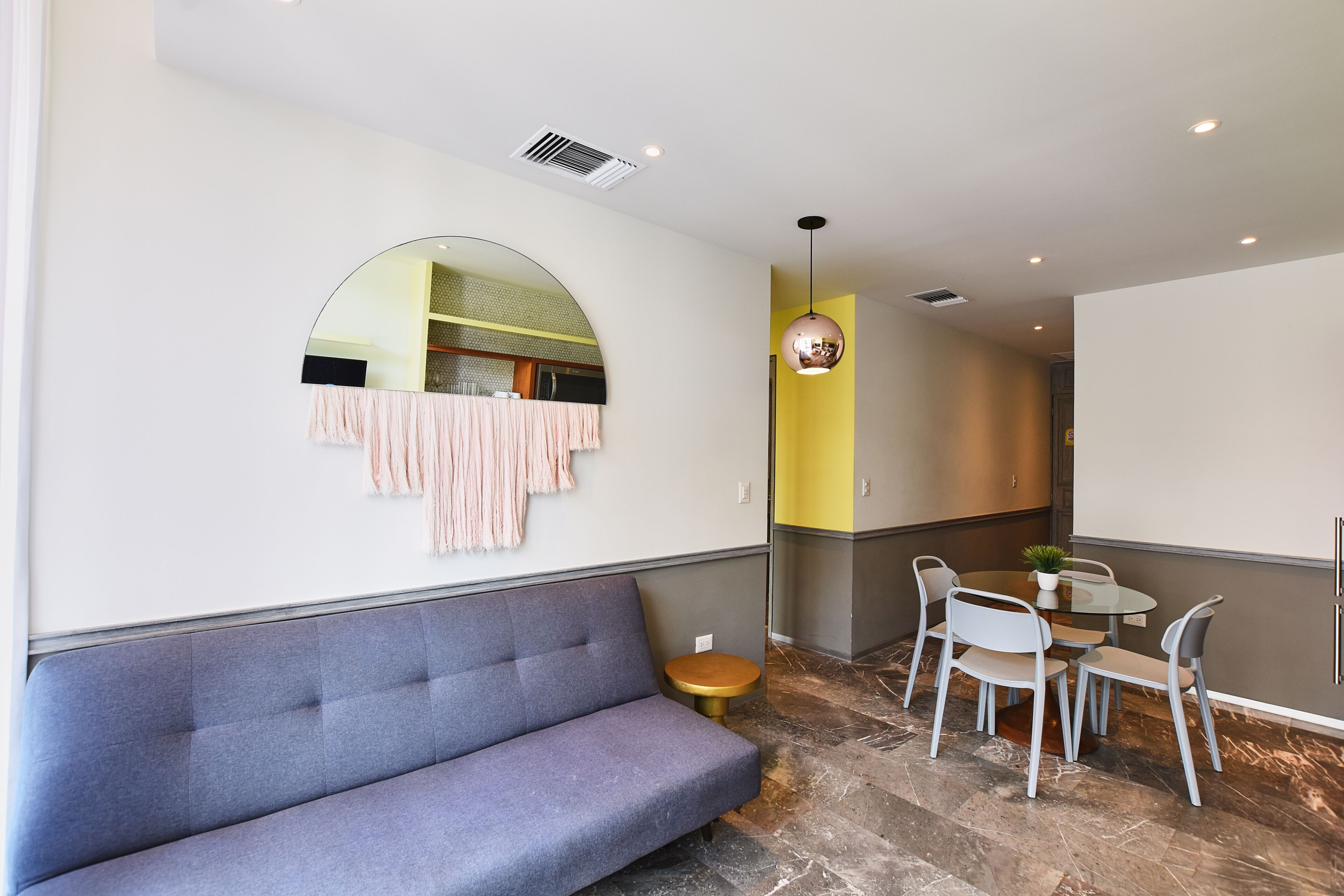 A modern interior with a grey sofa, a round mirror, a small round table, and a yellow accent wall.