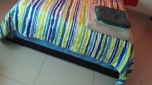Een bed met een gestreept dekbed, een nachtkastje met een lamp en een raam met oranje gordijnen.