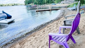 Een strand met een steiger, opblaasboten en strandstoelen.