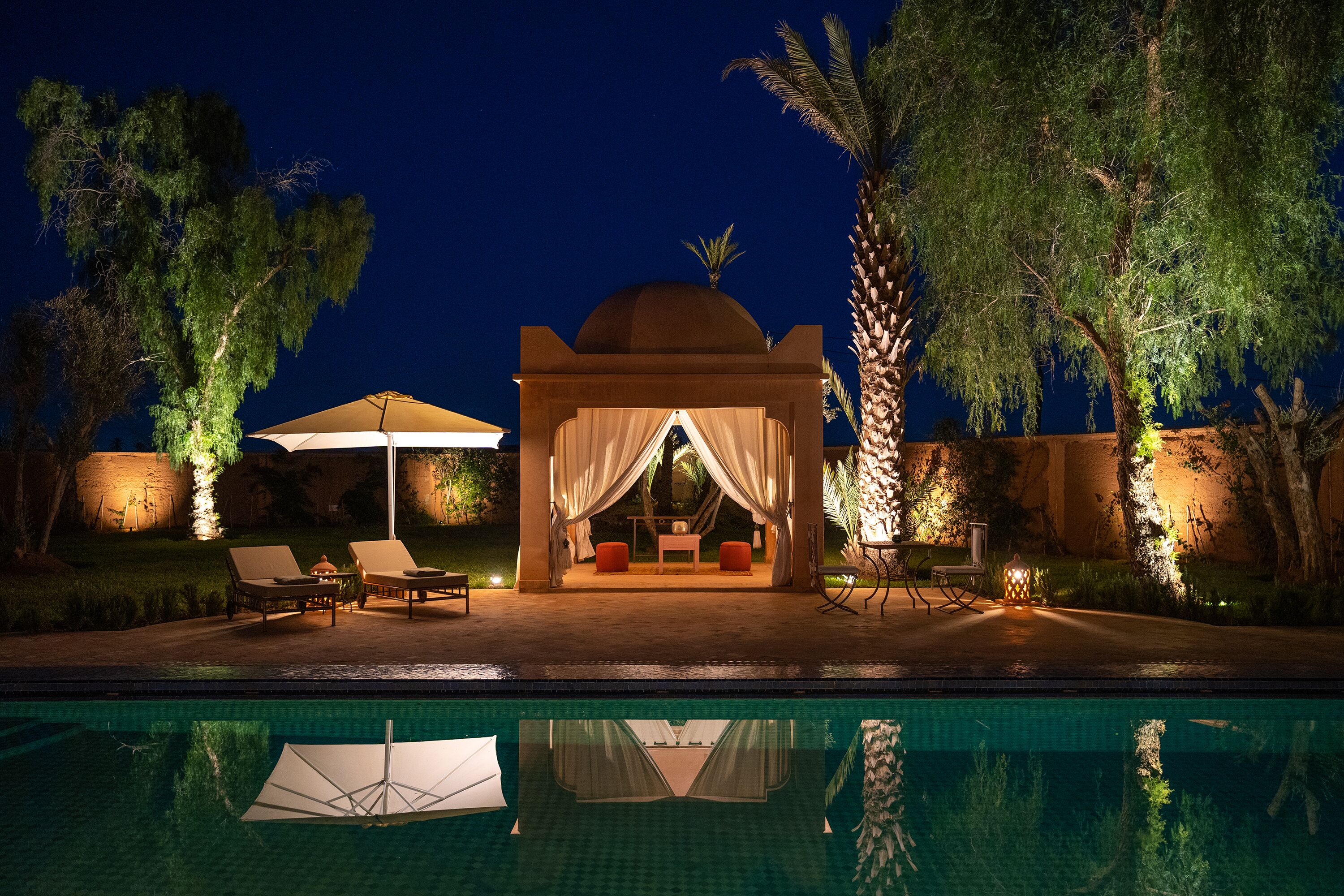 A poolside area with a covered seating area, lounge chairs, and a pool.