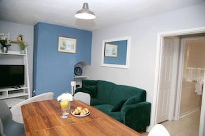 A dining area with a wooden table, chairs, a green sofa, and a TV on a shelf. - Serene Haven 4-bed House in Norwich (Norwich)