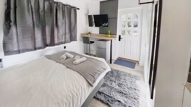 Ett sovrum med en säng, ett skrivbord, en stol, en tv och en dörr med ett fönster.