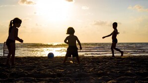 Tre bambini giocano a calcio su una spiaggia al tramonto.