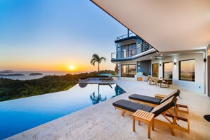 A modern house with a swimming pool, lounge chairs, and a dining area with a view of the sunset and landscape. - Serene Villa Ocean View Pool Rooftop Deck 5 BR - Villa Vista Pacifico (Tempate)