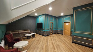 Un salon chaleureux avec un mur en briques sombres, des murs d’accent de couleur turquoise, un canapé en cuir marron, des fauteuils rouges et un plancher en bois.
