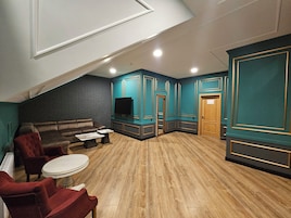 A cozy living room with a dark brick wall, teal accent walls, a brown leather sofa, red armchairs, and a wooden floor.