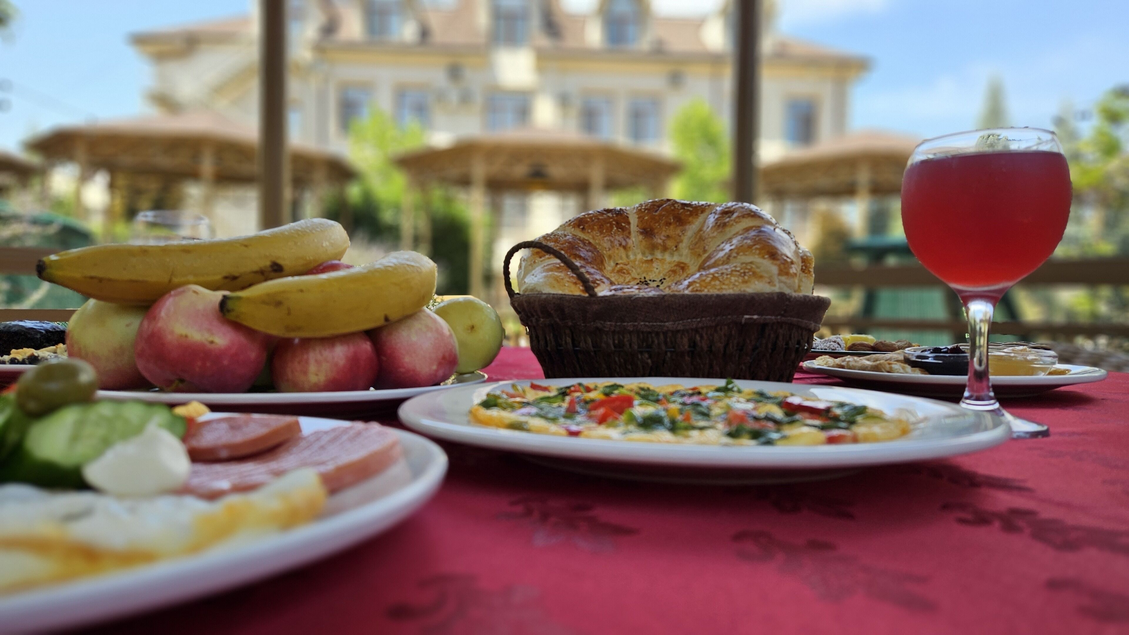 A breakfast table with various foods, including fruits, bread, and a drink, set outdoors with a building in the background.