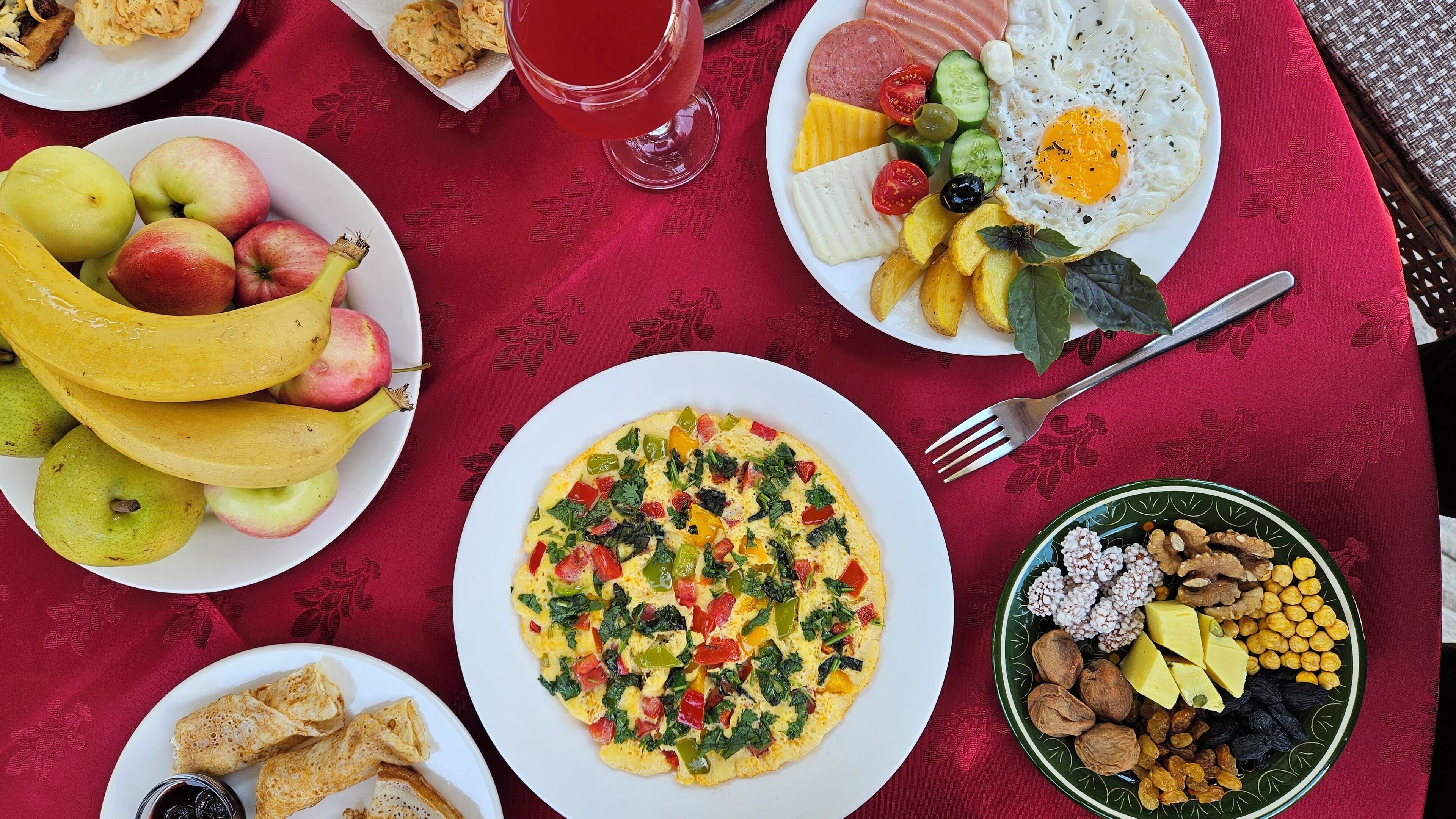 Un esmorzar abundant amb diferents plats, com ara ous, fruita i pastissos, damunt d'un mantell vermell.