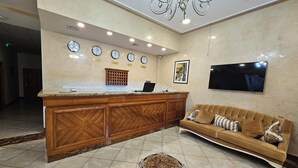 Un espace d’accueil comprenant un comptoir de réception en bois, un canapé, un lustre, des horloges et un téléviseur.