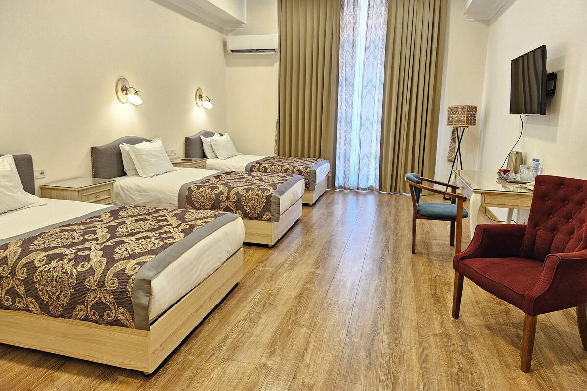 Ein Hotelzimmer mit zwei Betten, einem Schreibtisch, einem Stuhl, einem Fernseher und einer Klimaanlage.