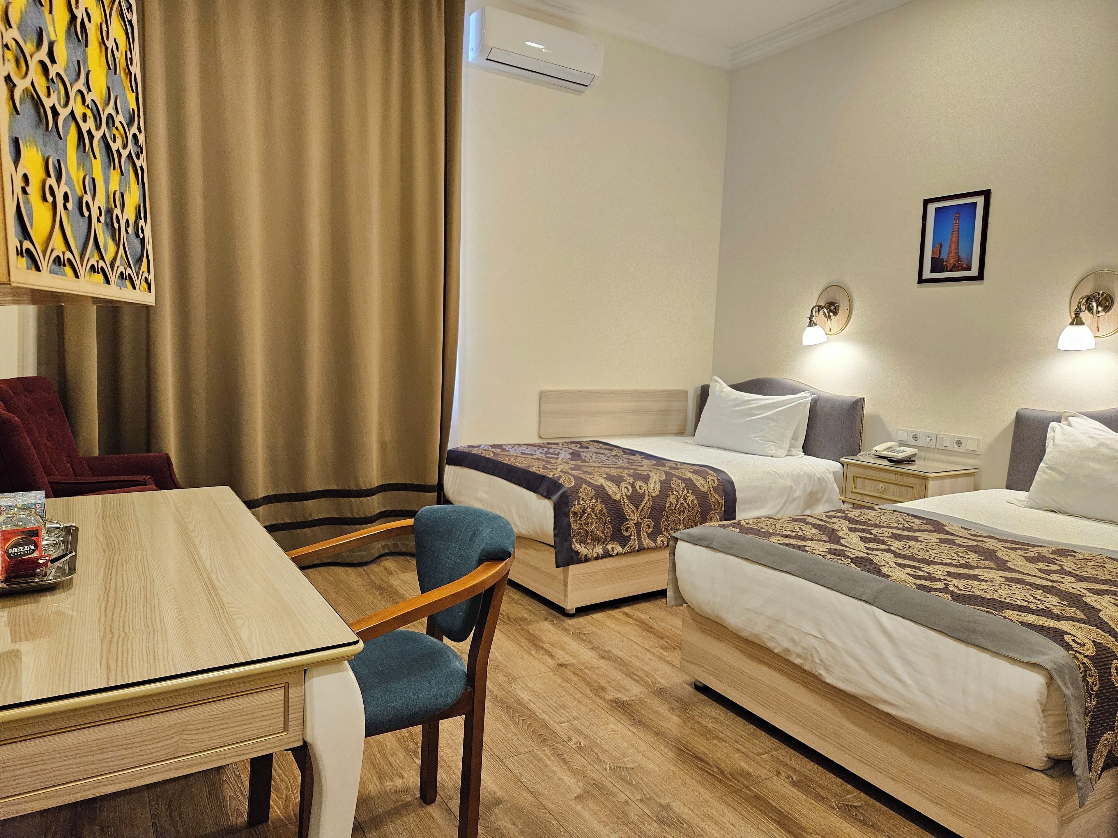 Ein Hotelzimmer mit zwei Betten, einem Schreibtisch, einem Stuhl, einem Tisch und einer Wand-Klimaanlage.