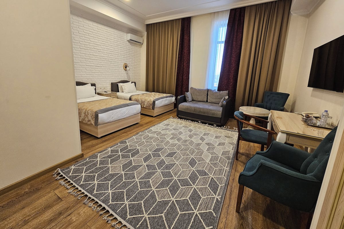 Ein Hotelzimmer mit zwei Betten, einer Couch, einem Esstisch und einem an der Wand befestigten Fernseher.
