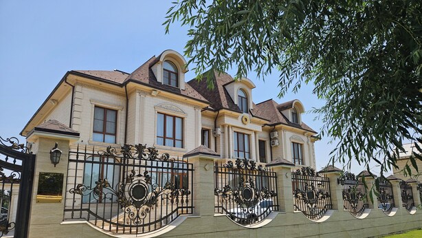 Un grand bâtiment historique à la façade symétrique, agrémenté de grilles en fer forgé décorées et doté d’une pelouse bien entretenue.