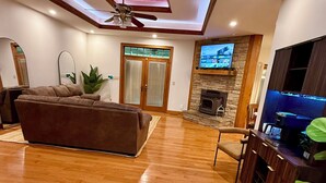 Uma sala de estar ampla com piso de madeira, um sofá grande, uma TV fixada em uma parede de pedra e um ventilador de teto.