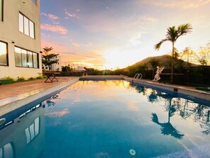 Una piscina con vistas despejadas al atardecer, un edificio moderno y una estatua.