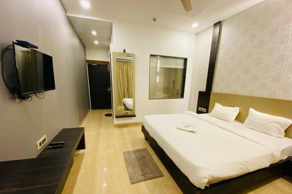 A hotel room with a bed, a TV, a mirror, and a window.