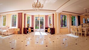 A spacious living room with a large sofa, a dining area with a table and chairs, and a view of the outdoors through large windows.