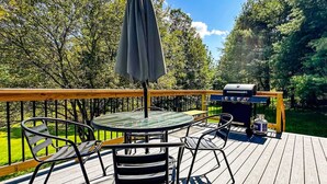 Une terrasse avec une table ronde et des chaises, un barbecue et une bouteille de gaz.
