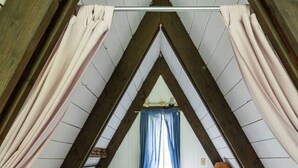 Une chambre à coucher avec un plafond en pente, un lit, une table de chevet, une lampe et une fenêtre avec des rideaux.