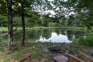 Surround yourself with nature's serenity by the tranquil pond, where a rustic fire pit and wooden benches invite relaxation.