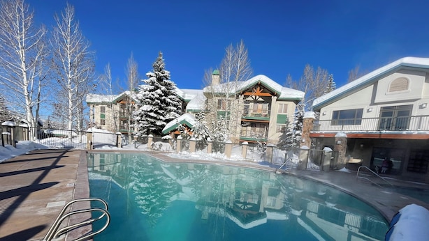 A pool area with a clear blue pool, surrounded by buildings with snow-covered trees and a clear sky. -  Modern Mountain Retreat - Ski-in-out - Heated Pool and Hot Tub (Steamboat Springs)