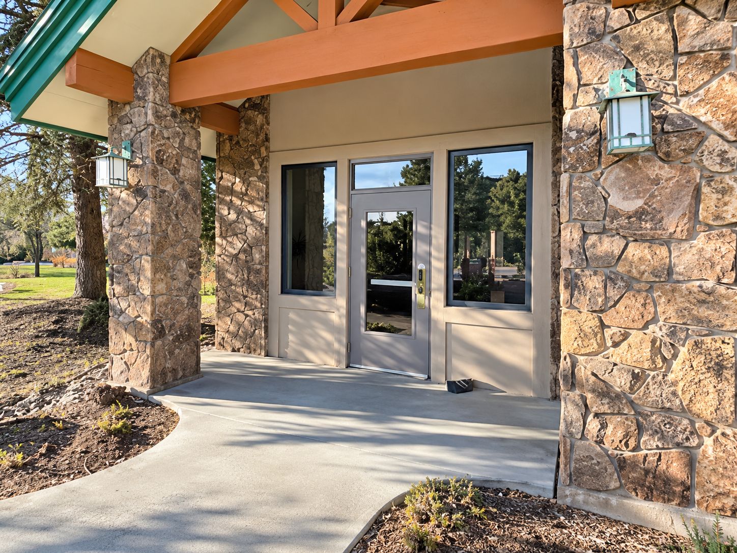 A building entrance with a stone facade, a door with a window, and a pathway leading to the entrance.