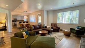 A spacious living room with a sectional sofa, a coffee table, and a dining area with a table and chairs. A kitchen is visible in the background, and there are large windows providing natural light. -  Modern Mountain Retreat - Ski-in-out - Heated Pool and Hot Tub (Steamboat Springs)